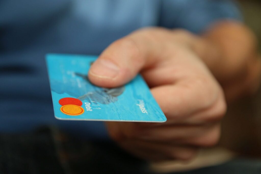 A close up of a single hand offering a blue mastercard to the camera 