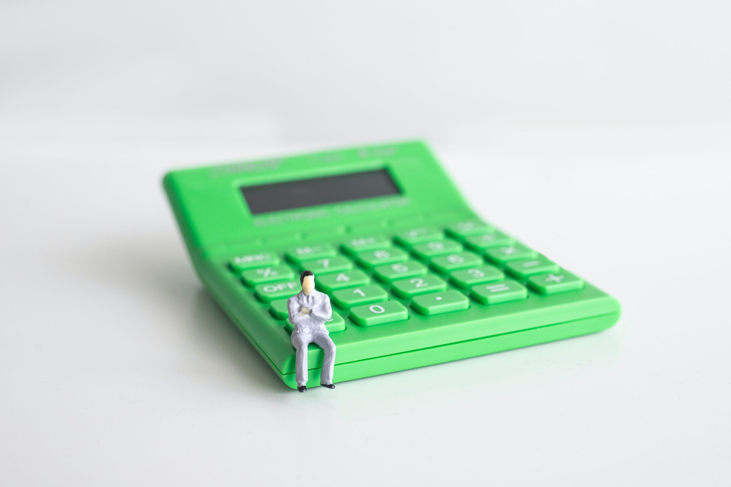 miniature man sitting on a green calculator