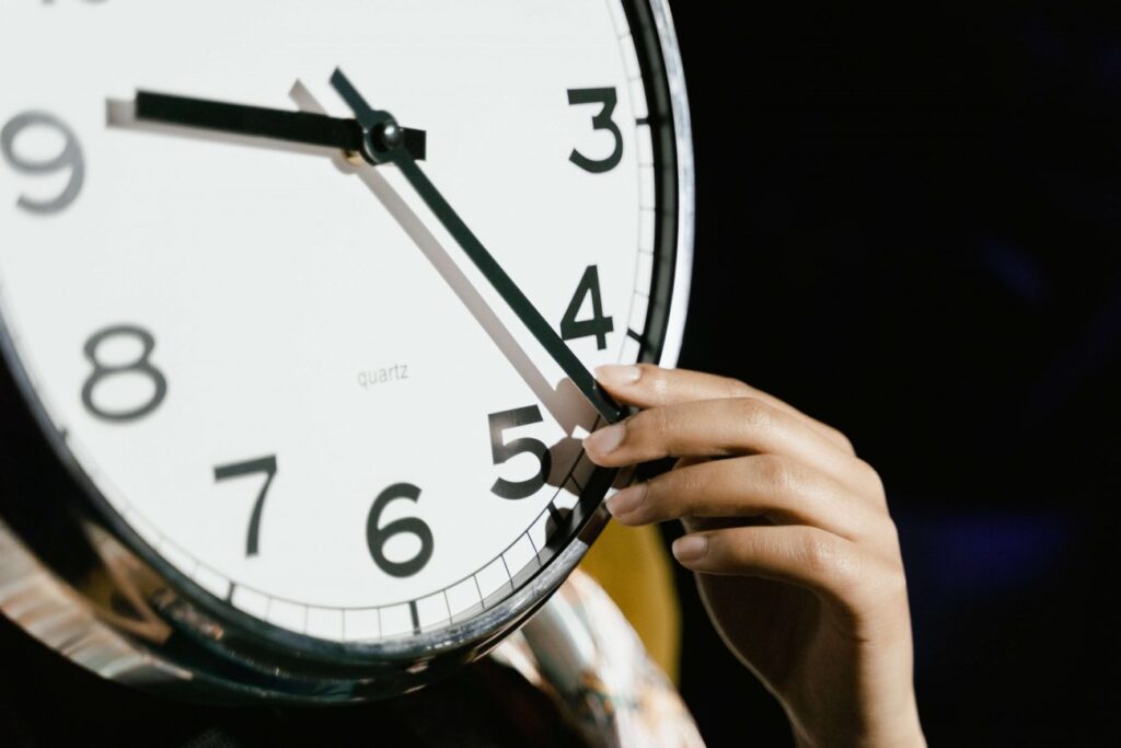 A large white clock face with a woman's hand reaching around from the back to make an adjustment