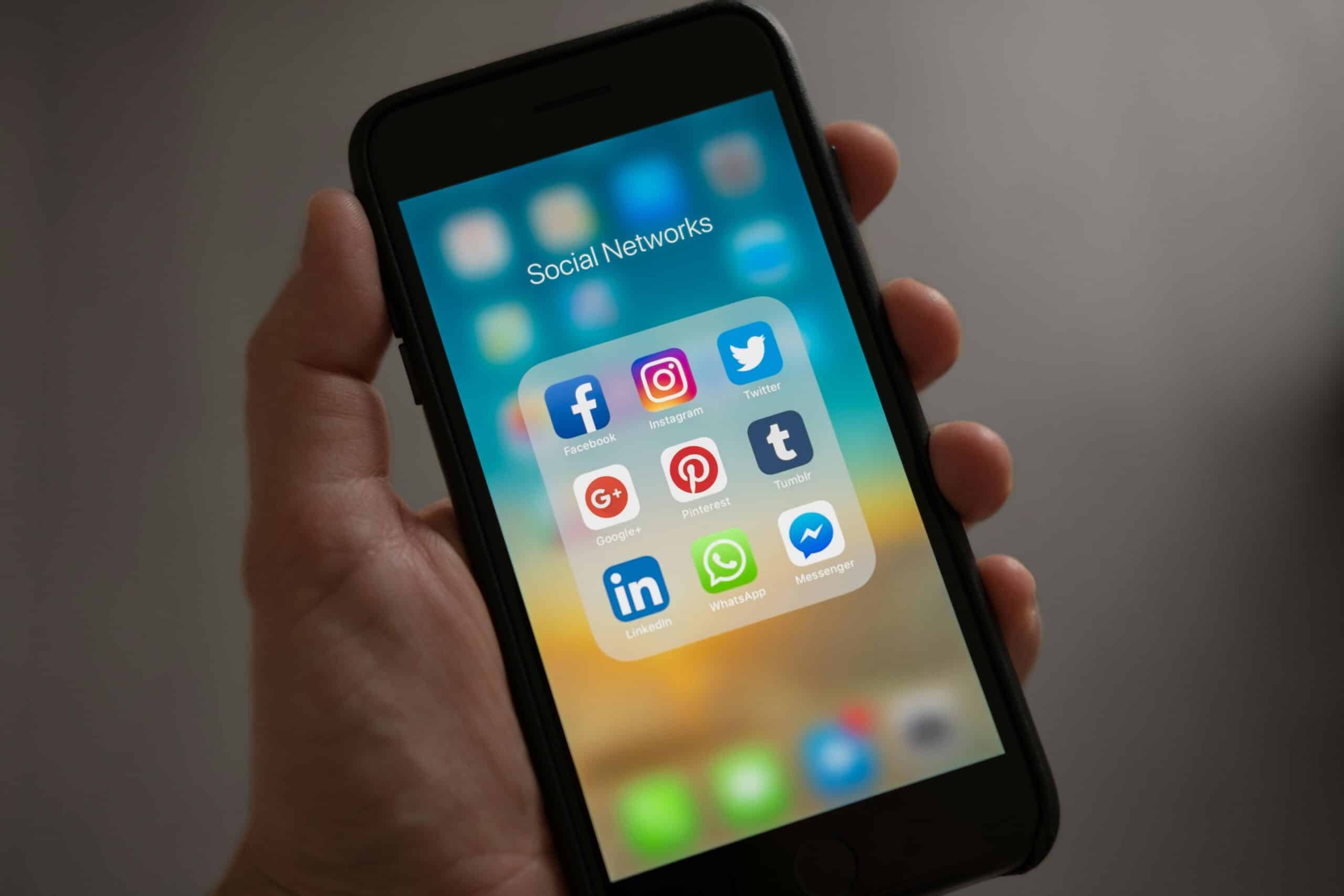 A hand holding a smartphone with a screen showing many different social apps