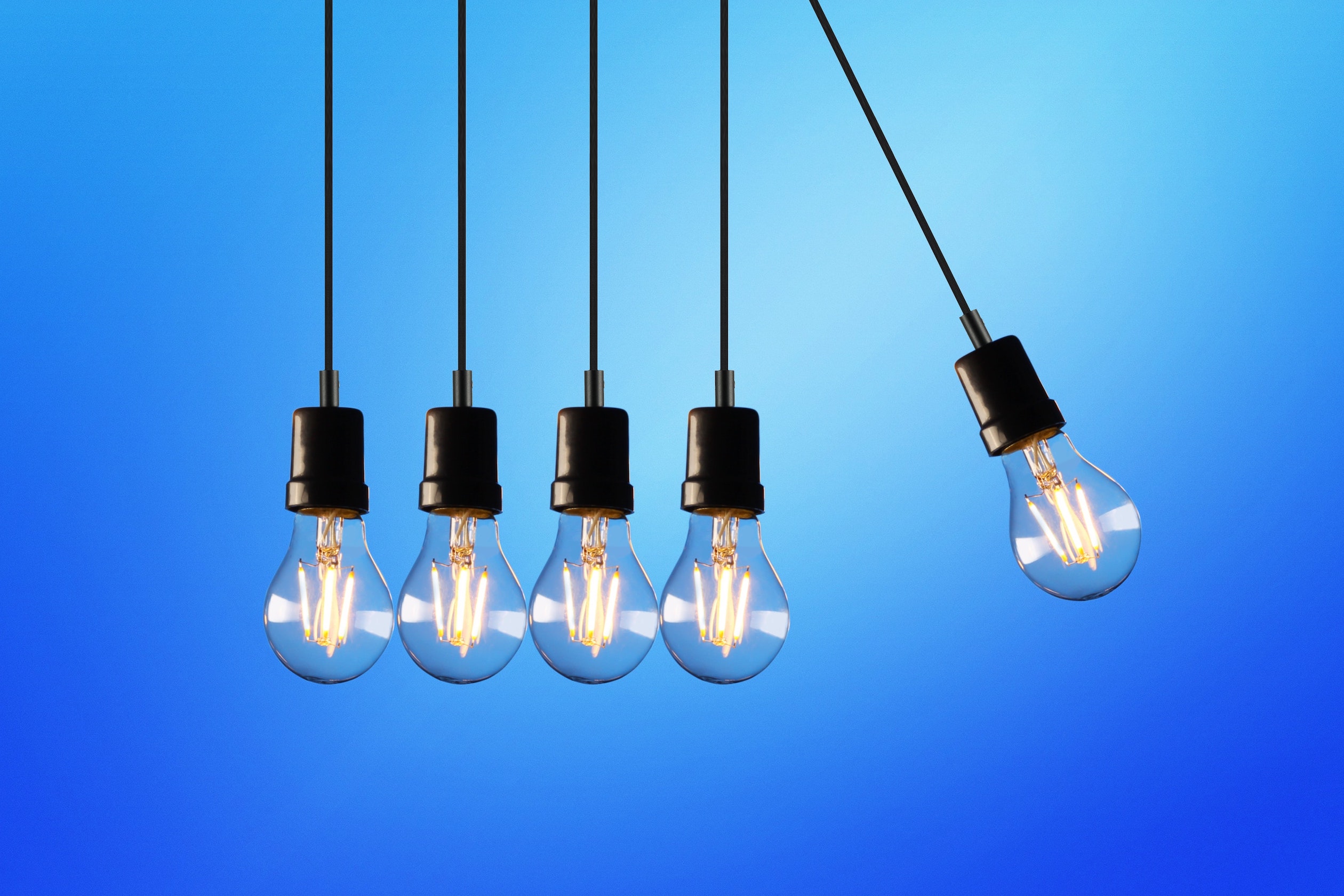 five bare lightbulbs with one swinging towards the other 4 against a blue background