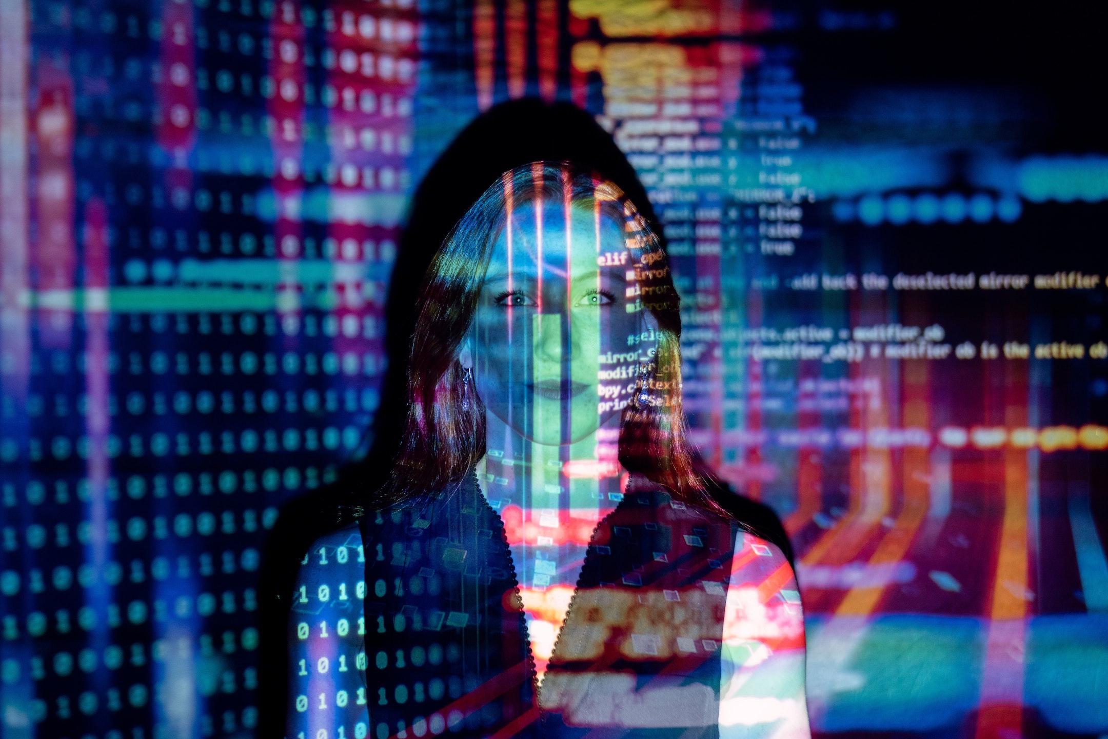 Woman's face in front of a screen with computer code projected on her face
