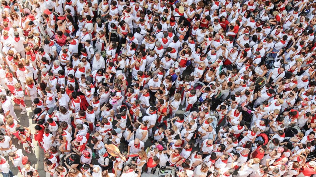 An overhead view of hundreds of attendees at a Spanish or Basque outdoor festival all dressed in matching white and red 