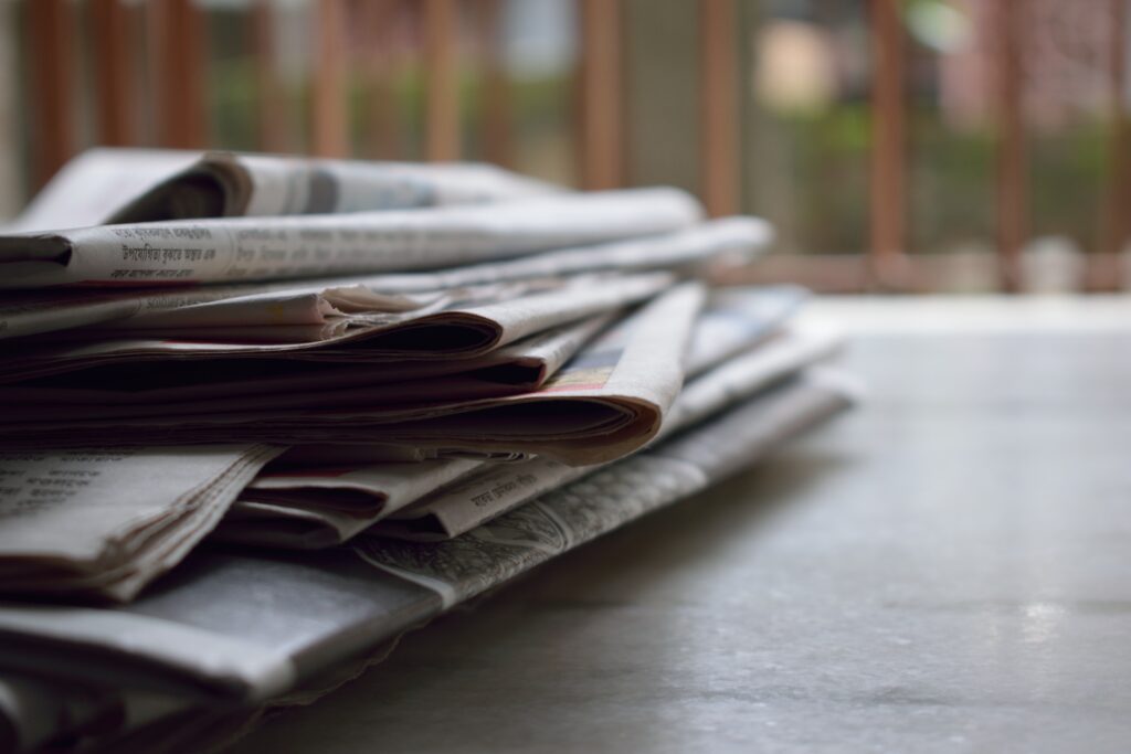 A close-up of loosely stacked newspapers on an outdoor table with a blurred background.