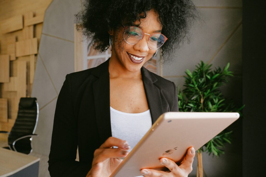A dark haired young woman standing and interacting with her ipad with a smile on her face