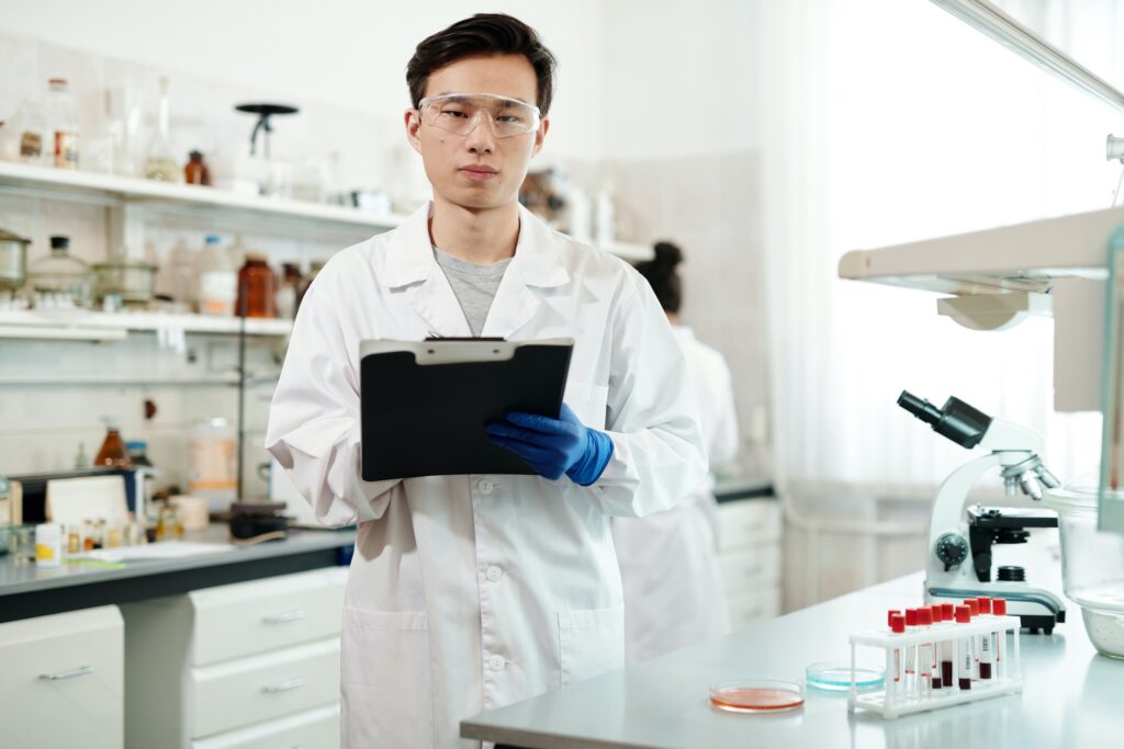 A man scientist writes on a clipboard in a lab.
