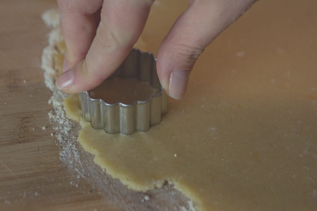 A womans hand pressing a cookie cutter in to cookie dough