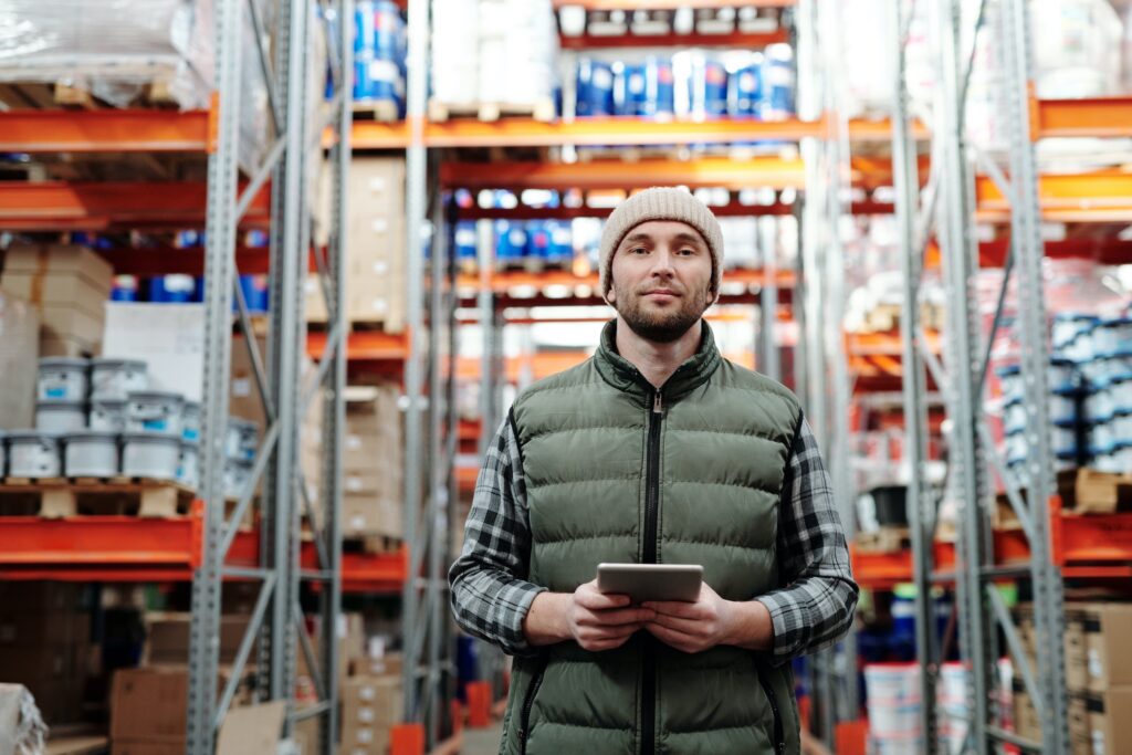 Male warehouse worker in a green sleeveless vest holding a tablet