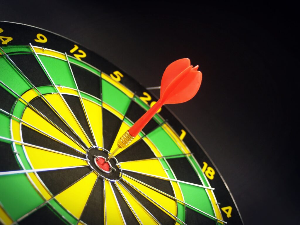 A bright yellow, black and green target with a red dart in the small red center ring