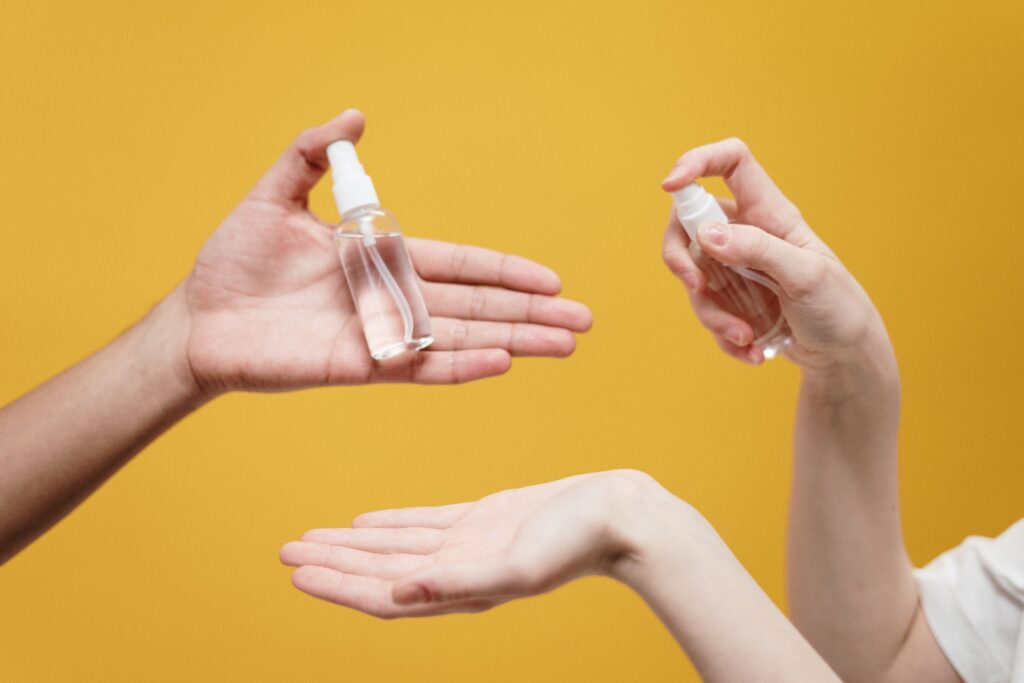 Disembodied hands holding and spraying hand sanitiser against a yellow background