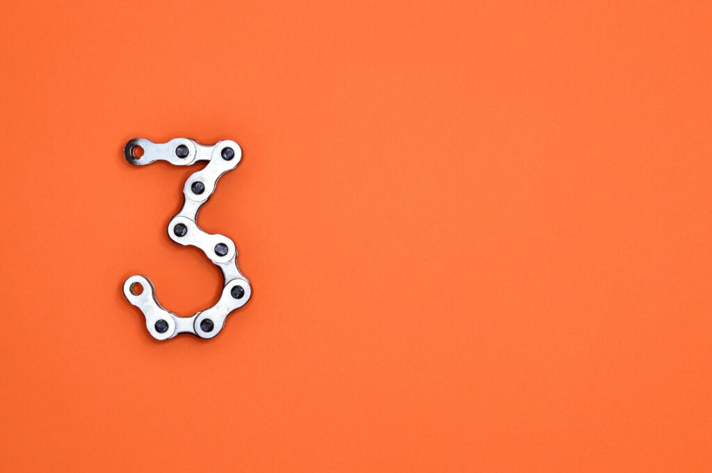 The number "3" made up of bicycle chain links against an orange background