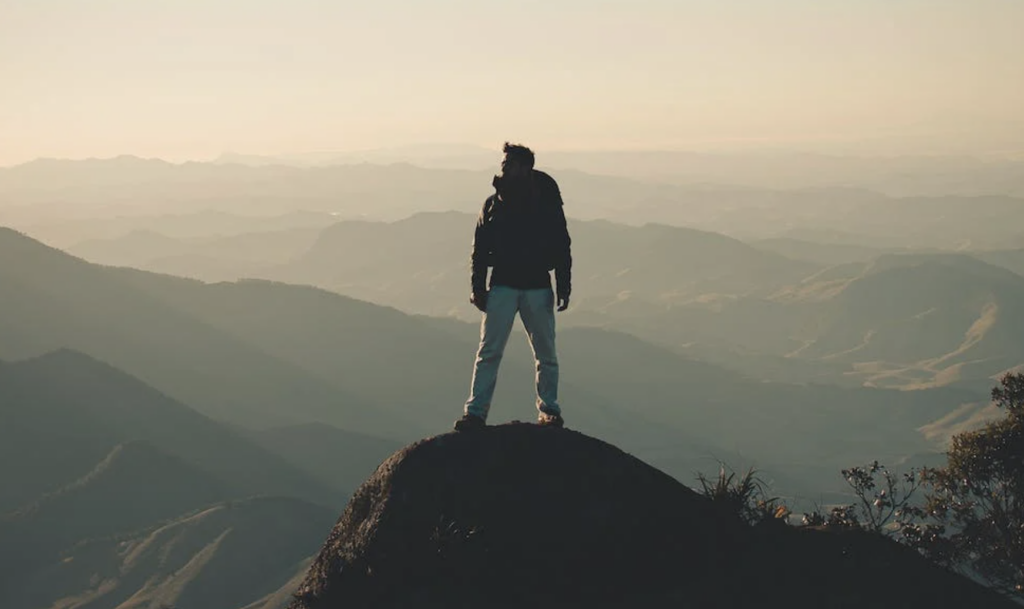 A man on top of a peak looking out over a series of mountain ranges 