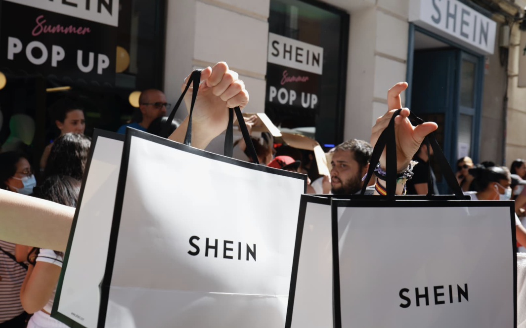 Shoppers holding up white and black Shein shopping bags outside of a Shein pop up store