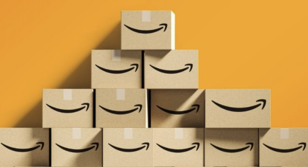 A pyramid of cardboard Amazon boxes with the smiling underlined Amazon logo against a yellow background 