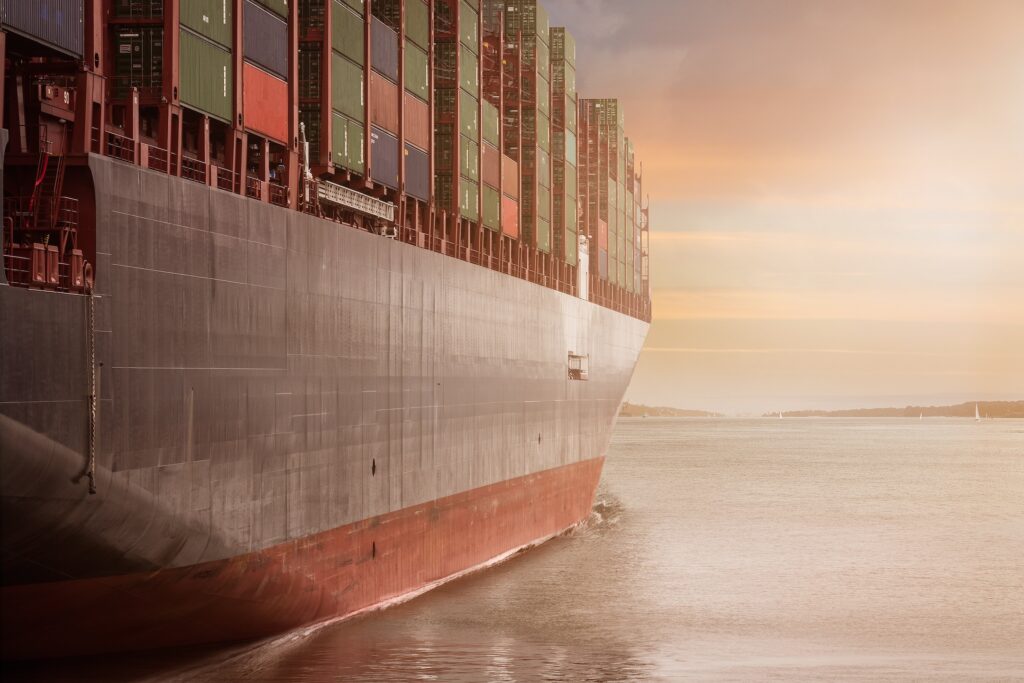 A view of an enormous, fully loaded container ship moving diagonally away from the viewer. 