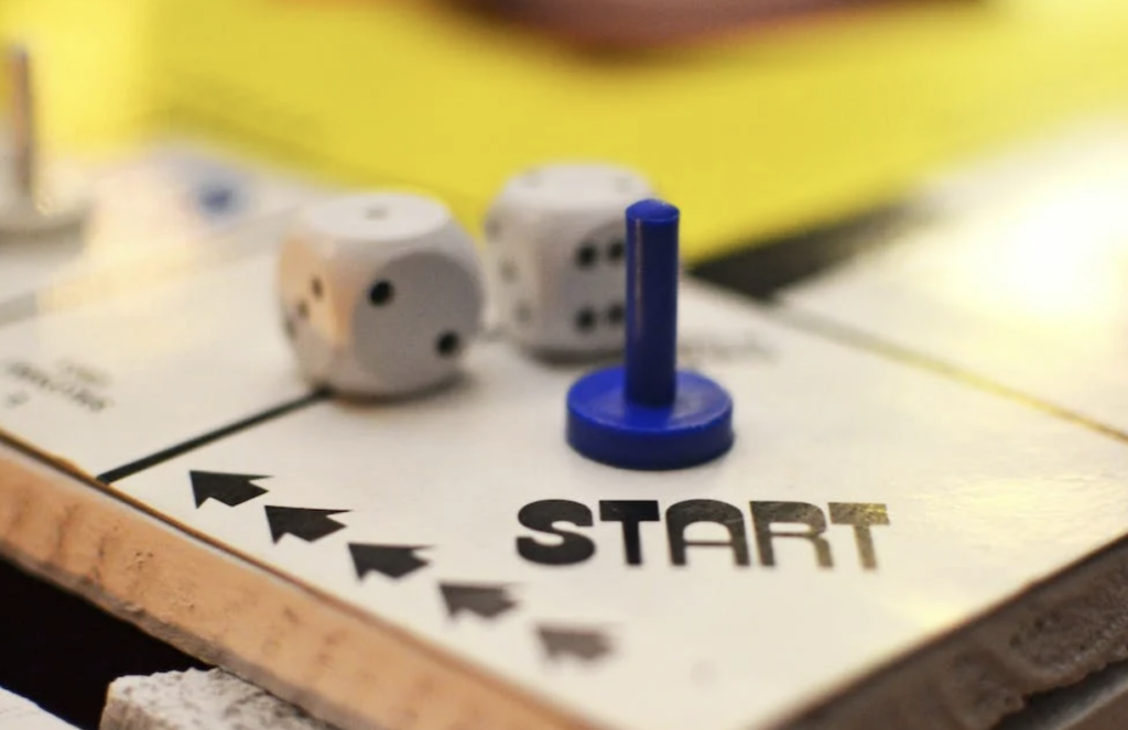 A close up of the start square of a board game with two dice and a single blue cylindrical character