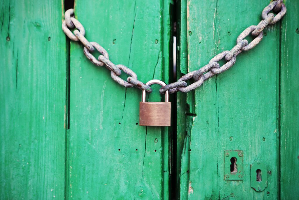A bright green wooden gate locked with a silver chain and a brass colored padlock