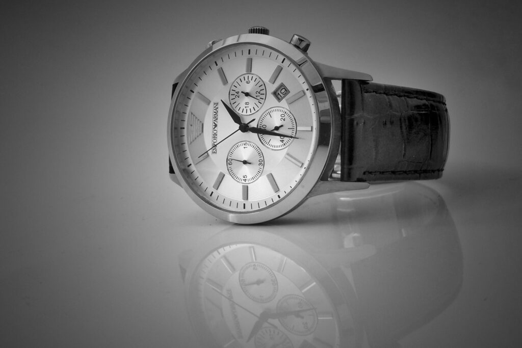 A close up, black and white photo of a mens dress watch posed on a shiny table 