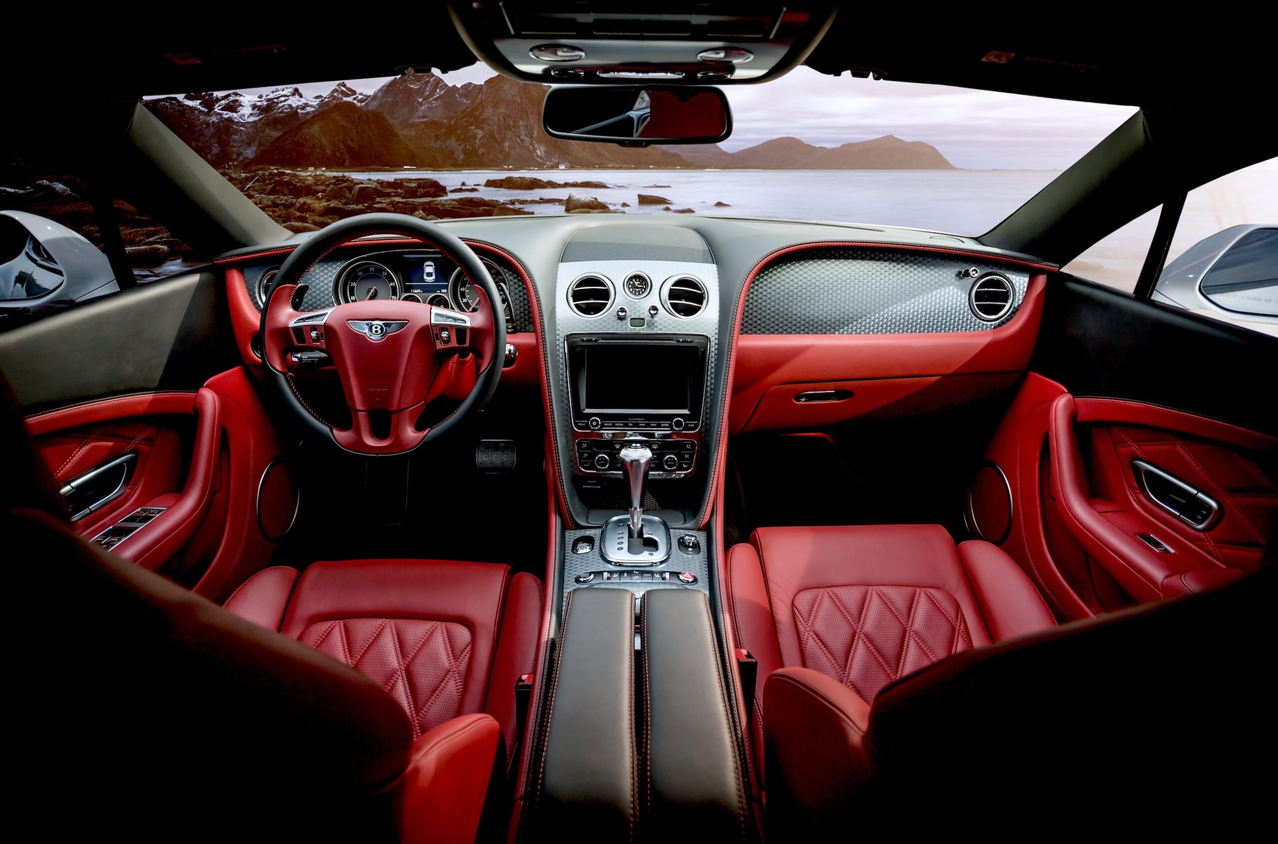 The red leather interior of a beautiful Bentley automobile, looking out onto an ocean front view