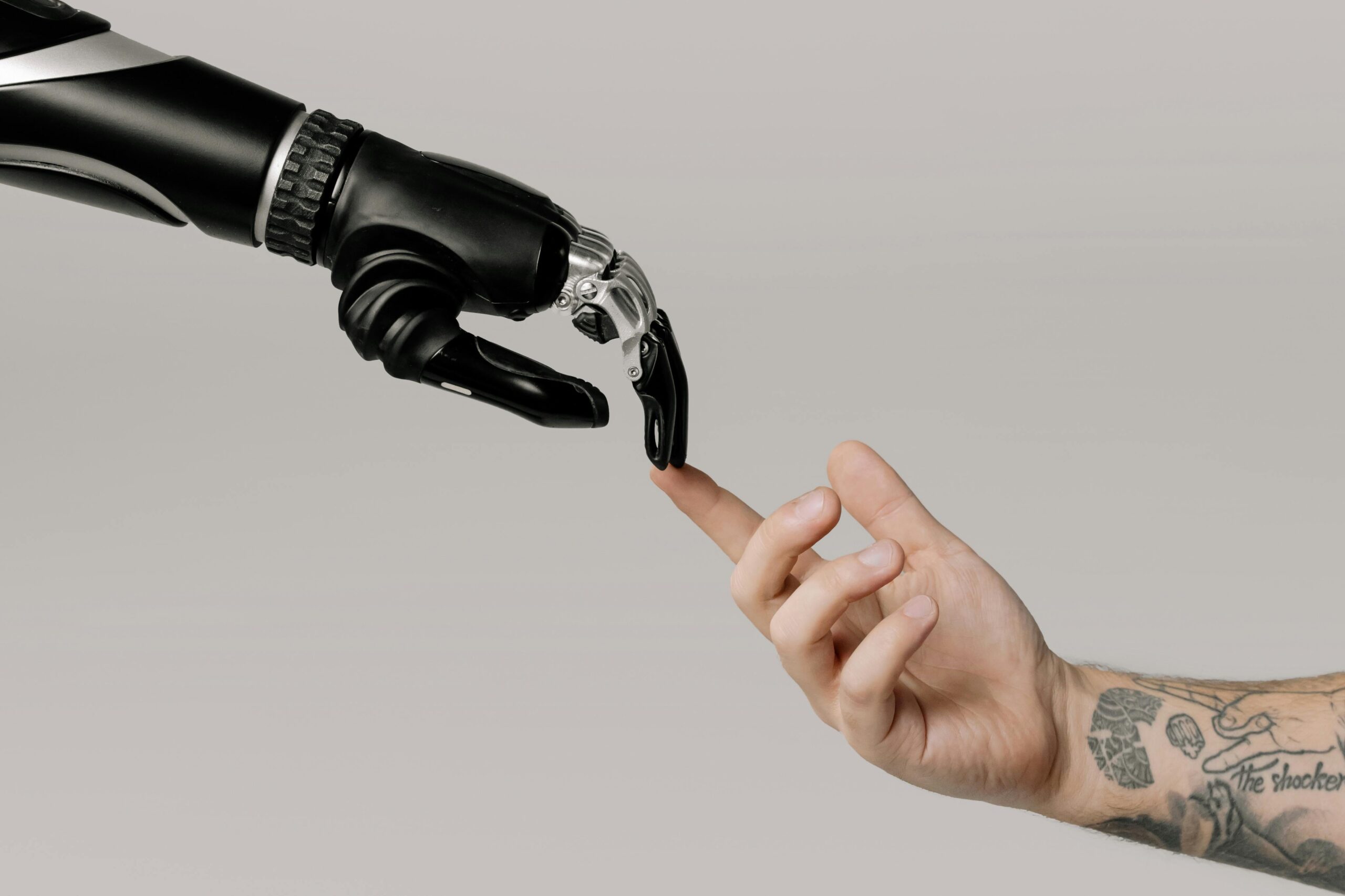 an outstretched robot hand touching a tattooed human hand