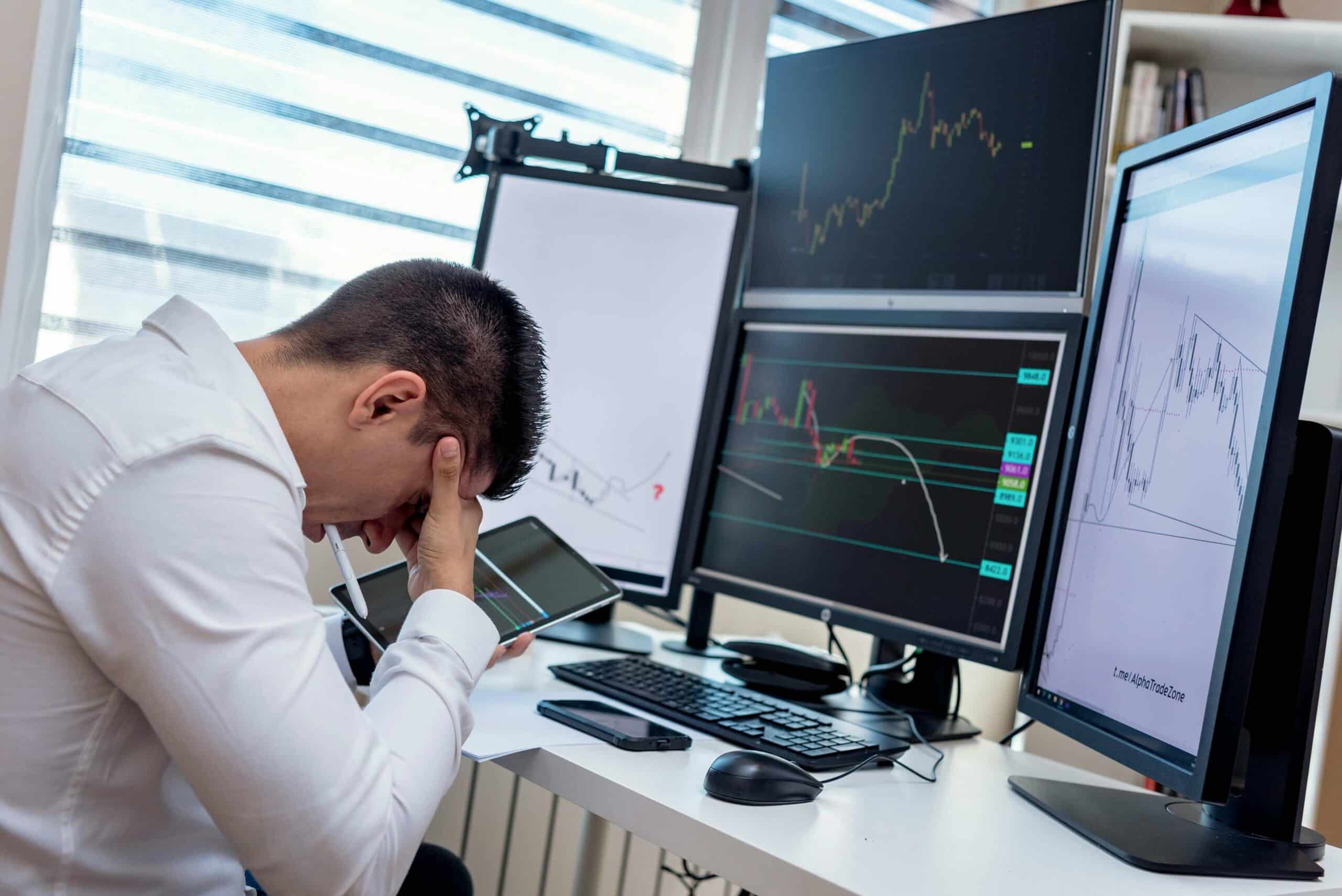 Ecommerce professional with his head in his hands looking at a desktop computer showing downward trending business charts